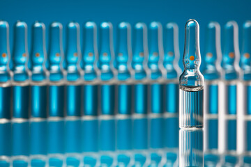 Medical glass ampoules with vaccine on a blue background. Shallow depth of field. Selective focus on one ampoule.