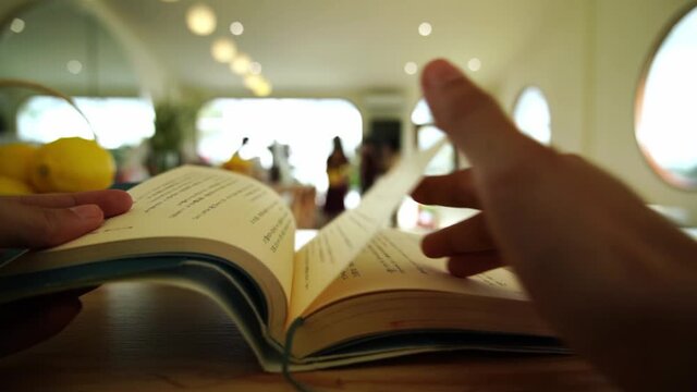 The hand of a person opening a book to read in a cafe in the morning._Slow motion.