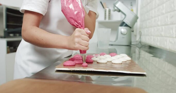 Making Pink Macarons. Piping Out Pink Macaron Mixture On A Slip Mat On Backing Tray, Chef Making Macarons With Piping Bag. Female Young Confectioner Making Macarons In Her Cozy Light Pastry Shop.