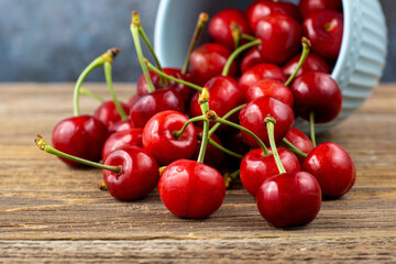 Ripe wet sweet cherries are poured out of the blue bowl on wooden