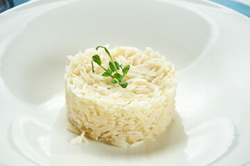 Delicious side dish for main courses - boiled rice with microgreen in a white plate on a blue tablecloth. Close up view