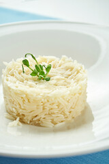 Delicious side dish for main courses - boiled rice with microgreen in a white plate on a blue tablecloth. Close up view