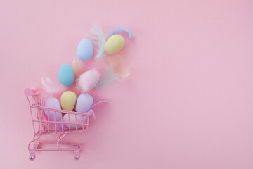 Easter sale background. Shopping cart with colorful easter eggs on pink background.