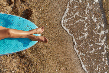 Holiday trip, summer time and time to relax idea, copy space. Womans legs getting tanned on sun. Wet sand on coastline.