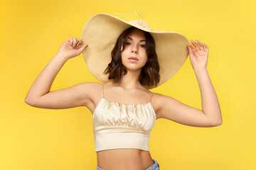 beautiful tanned young woman in summer hat on yellow background.