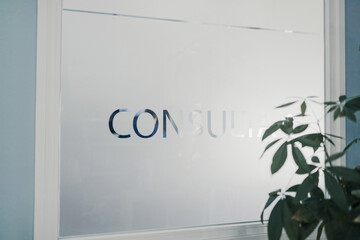 Consultant title on door with opaque glass near green plant in clinic in daytime