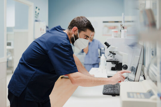 Side view of crop anonymous male medic in uniform and mask using microscope while working in lab