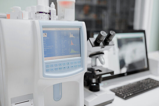 Hematology analyzer with graphs on monitor near microscope and desktop computer with images on screen in lab
