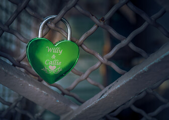 Close detail of shiny engraved green "love lock" - as worldwide tradition to resilient and everlasting love. Female's and male's name on the top. Selective focus.