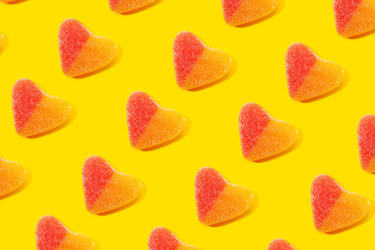 Top view flat lay composition of multicolored jelly candies in shape of heart arranged in rows on yellow background