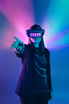 Unrecognizable female with outstretched arm wearing VR headset while exploring virtual reality under blue neon light