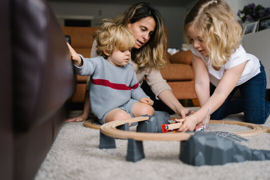 Young woman with little son and daughter playing with toy road and cars on carpet while spending free time together at home