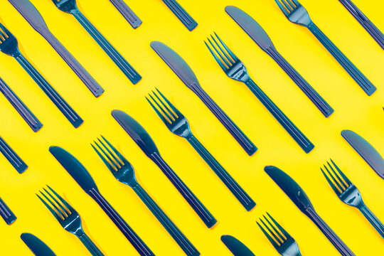 Top view full frame of disposable plastic forks and knives arranged in order on yellow background