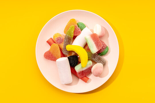 Top view of yummy multicolored gummy candies on striped plate placed on yellow background - Powered by Adobe