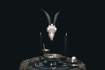 Witchcraft composition with animal skull, candles, magic book and pentagram symbol. Altar for satanic rituals. Black magic and occult objects.
