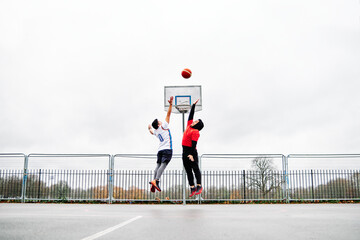 Young male friends playing basketball at the court, jumping by the hoop.