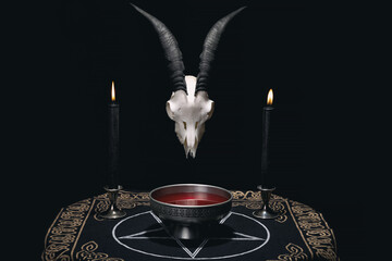Altar for satanic rituals. Witchcraft composition with goat skull, pentagram cloth, candles and ritual bowl with blood. Occult and esoteric concept.
