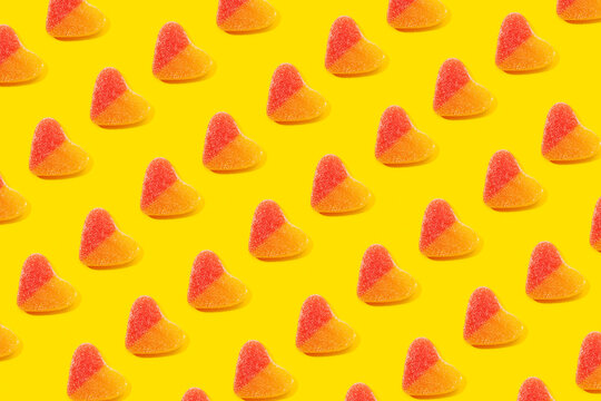 Top view flat lay composition of multicolored jelly candies in shape of heart arranged in rows on yellow background