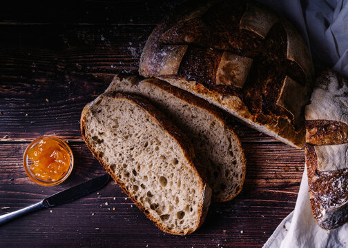 Top view of slices of baked bread placed on wooden table in kitchen with knife and sweet homemade jam in glass bowl