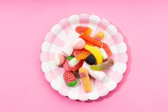 Top view of yummy multicolored gummy candies on striped plate placed on pink background