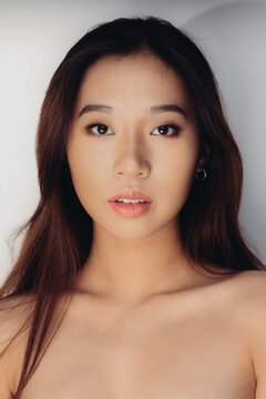 Portrait Of Naked Young Chinese Woman Looking At Camera Over White Background