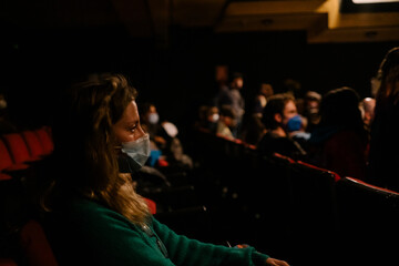 woman with mask watching a show in a theater keeping sanitary measures