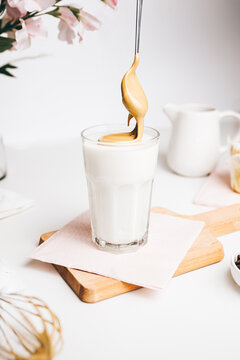 Teaspoon with sweet whipped foam above fresh yummy latte served on wooden cutting board in modern light kitchen