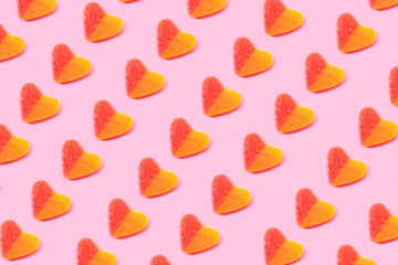 Top view flat lay composition of multicolored jelly candies in shape of heart arranged in rows on pink background
