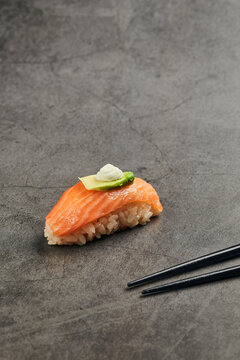 High angle of palatable nigiri sushi with slice of salmon on rice topped with thin slice of avocado and cream cheese served near chopsticks