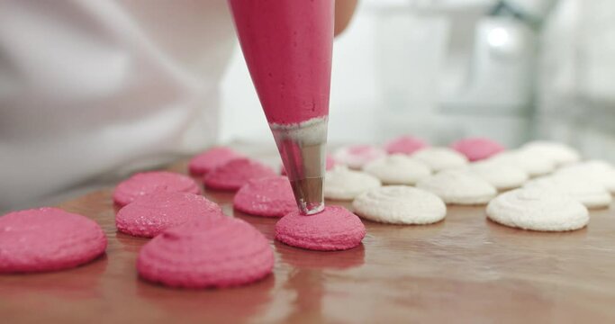 Piping Out Pink Macaron Mixture On A Slip Mat On Backing Tray, Chef Making Macarons With Piping Bag. Female Young Confectioner Making Macarons In Her Cozy Light Pastry Shop. Making Pink Macarons.