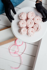 pink meringue on a white plate and hands of a pastry chef in black gloves