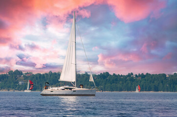 Obraz premium Sailing yachts sail under a beautiful evening sky with pink clouds.