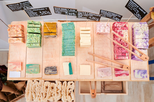 From above of various colorful handmade soap with tongs and price tags placed on wooden table in eco store