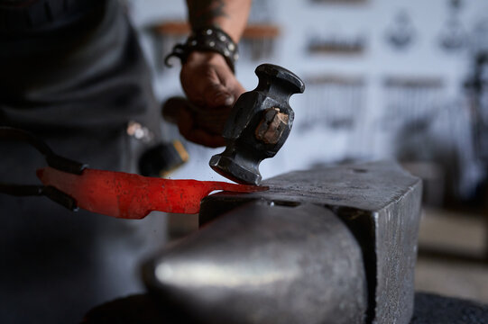 Side view of anonymous tattooed young male forger in apron heating metal in furnace while working in grungy smithy