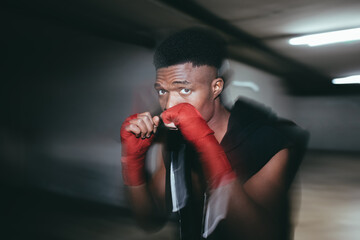 Young strong African American sportsman in boxing hand wraps working out and looking at camera in building