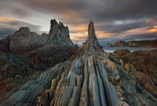 Long exposure sunset on the row of sharp stone islets emerging from the ocean, remains of an ancient fractured point of quartz and slate. This area is called La Forcada, from the famous Gueirua beach