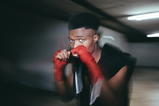 Young strong African American sportsman in boxing hand wraps working out and looking at camera in building