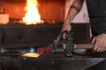Side view of anonymous tattooed young male forger in apron heating metal in furnace while working in grungy smithy