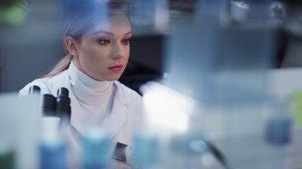 Female doctor working in laboratory. Studying medical samples. Looking through glassware and monitor