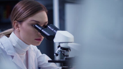 Female doctor working in laboratory. Studying medical samples. Looking through glassware and monitor