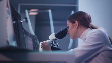 Female doctor working in laboratory. Studying medical samples. Looking through glassware and monitor