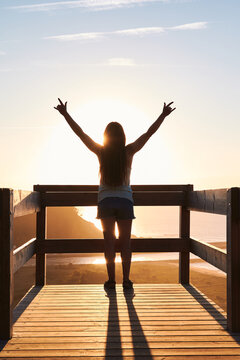 Bide view of female tourist standing on wooden terrace and admiring picturesque scenery of endless sea at sunset