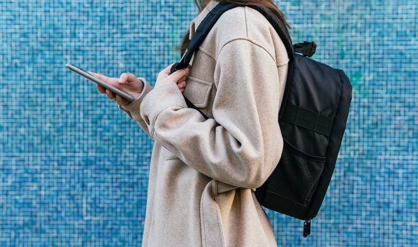 Side view of unrecognizable female student in casual wear with backpack standing against blue tiled wall
