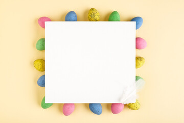 Minimal Easter flat lay composition from color Easter eggs and blank white canvas on pastel background. Top view, copy space for text