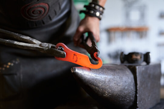 Side view of anonymous tattooed young male forger in apron heating metal in furnace while working in grungy smithy