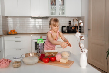 Mom and daughter cook in the kitchen. A young woman cooks with her child in the kitchen at home. Girls in pink clothes cook pizza. Happy and cheerful mom and daughter