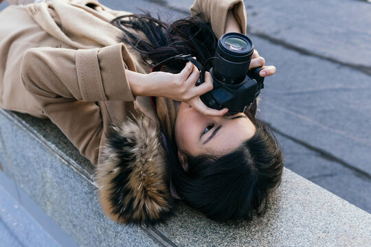 High angle of female photographer lying on stone parapet and shooting photo on professional photo camera