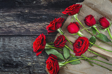 Top view composition of bright red blooming rose buds scattered on black surface with craft paper