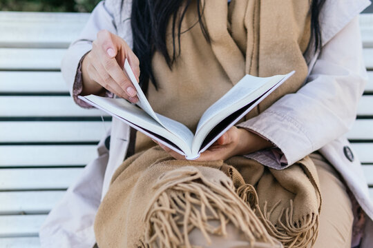 Cropped unrecognizable female reading book sitting in bench - Powered by Adobe
