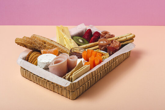 Brunch box with assorted sliced meats various types of cheese and crispbreads arranged near ripe cup kiwi sweet strawberries and peeled mandarin near jam in glass jar on colorful background